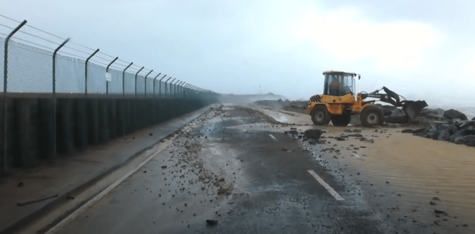 A digger clears away sand deposited on a Wellington Airport perimeter road after a recent storm